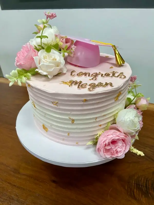 Pink and gold graduation cake with flowers and plastic cake